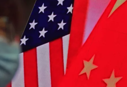 woman wearing a face mask to help curb the spread of the coronavirus sits near a screen showing China and U.S. flags