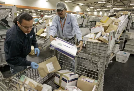 U.S. Postal Service mail handlers Alan Flores, left, and Romeo Gumpal sort packages.