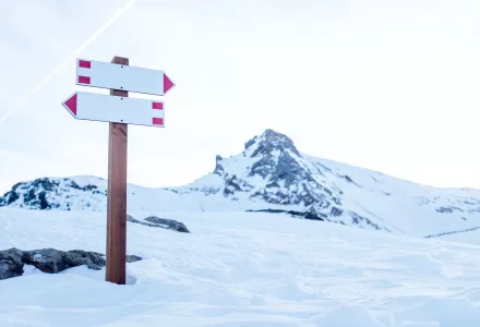 Two white signs indicating a path intersection in the mountains during winter.
