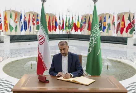 Hossein Amirabdollahian signs a register at the Saudi Foreign Ministry flanked by flags of Saudi Arabia and Iran.