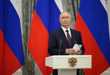 Russian President Vladimir Putin is standing against a wall with several Russian flags.