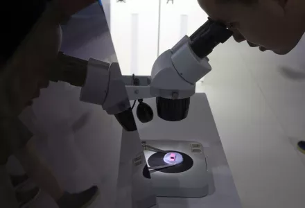 A visitor to the 21st China Beijing International High-tech Expo looks at a computer chip through the microscope displayed by the state-controlled Tsinghua Unigroup project which has emerged as a national champion for Beijing's semiconductor ambitions in Beijing, China, Thursday, May 17, 2018. The Trump administration has threatened to impose tariffs on up to $150 billion in Chinese imports to punish Beijing over trade practices requiring American companies to hand over technology in exchange for access to 