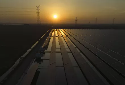 The sun sets over electric pylons along a solar farm 