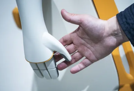 A human hand reaches out to shake the hand of a PAL robot.