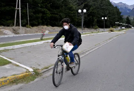 A man wearing a mask rides a bicycle on a street in Epuyen, Argentina, Friday, Jan. 11, 2019. An Argentine judge has ordered 85 residents of a remote Patagonian town to stay in their homes for at least 30 days to help halt an outbreak of hantavirus in which nine people have died. (AP Photo/Gustavo Zaninelli)