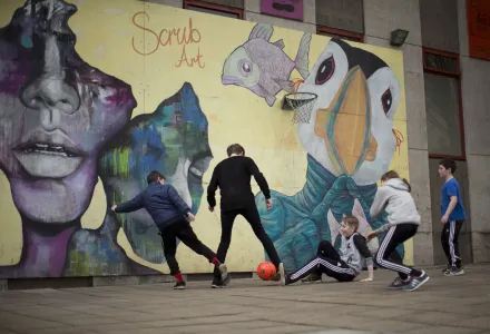 A youth worker and children at a youth center play soccer in front of a mural which includes a Puffin bird in Torshavn, Faroe Islands, Wednesday, March 18, 2015.