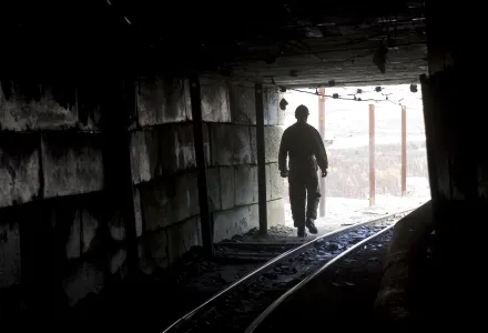 A miner is silhouetted at the mouth of a dark mine tunnel.