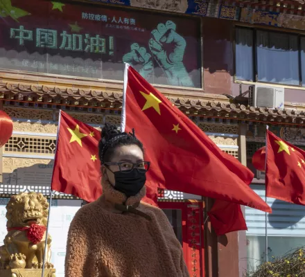 A masked woman walks past national flags and a government slogan which reads "Go China!" outside a traditional medicine hospital in Beijing on Tuesday, March 3, 2020. Mushrooming outbreaks in the Mideast, Europe and South Korea contrasted with optimism in China, where thousands of recovered patients were going home and new virus cases drop to a new low. (AP Photo/Ng Han Guan)
