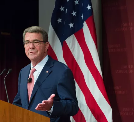 Ash Carter on the left of the picture speaking at a podium with an American flag in the background.