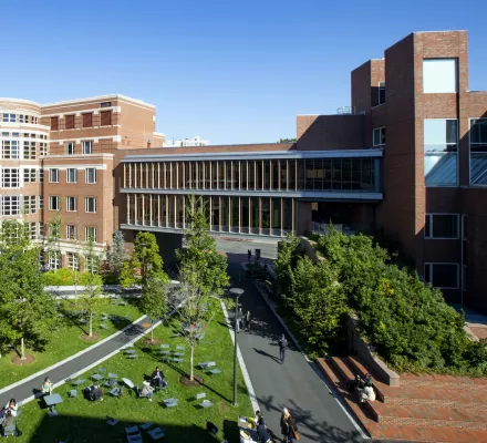A wide shot of the Harvard Kennedy School building and courtyard busy with students on a sunny, cloudless day.