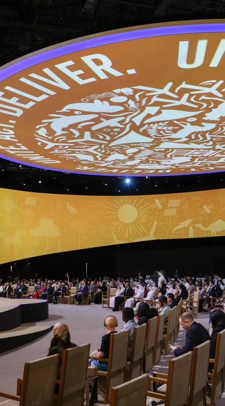 A large auditorium of people under a circular logo that reads "Unite. Act. Deliver." at the COP 28 summit. 