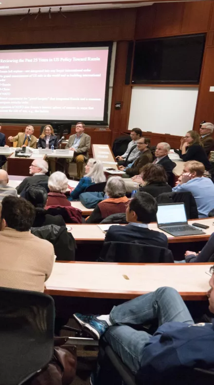 A wide shot of a packed auditorium, Graham Allison is gesturing to the audience.