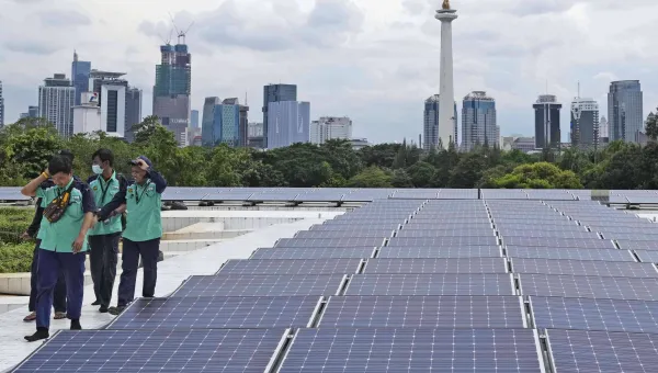 Workers walk near solar panels that provide partial electrical power to Istiqlal Mosque as the city skyline is seen in the background, in Jakarta, Indonesia, Wednesday, March 29, 2023. (AP Photo/Tatan Syuflana)