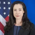 Headshot of Mallory Stewart with an American flag over a blue background
